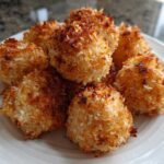A pile of golden brown, crispy Air Fryer Crispy Coconut Chicken Bites served on a white plate.