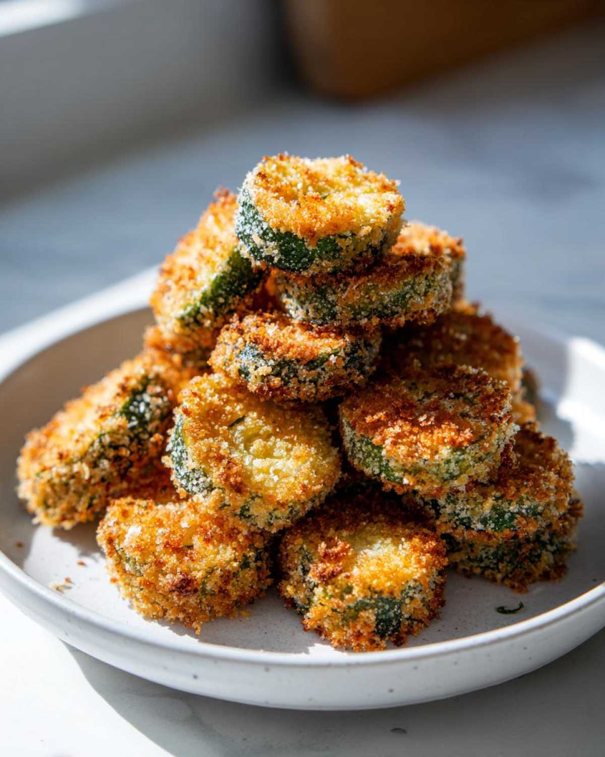 A stack of golden brown, breaded Air Fryer Crispy Garlic Dill Pickles slices piled high on a light-colored plate.