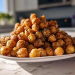A mound of golden brown Air Fryer Crispy Garlic Herb Chickpeas seasoned with visible rosemary pieces, served on a white plate.