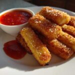A plate of golden brown Air Fryer Crispy Halloumi Fries sprinkled with salt, served with a side of red dipping sauce.