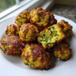 A pile of golden brown Air Fryer Crispy Parmesan Broccoli Tots on a white plate, one is broken open showing the green broccoli interior.