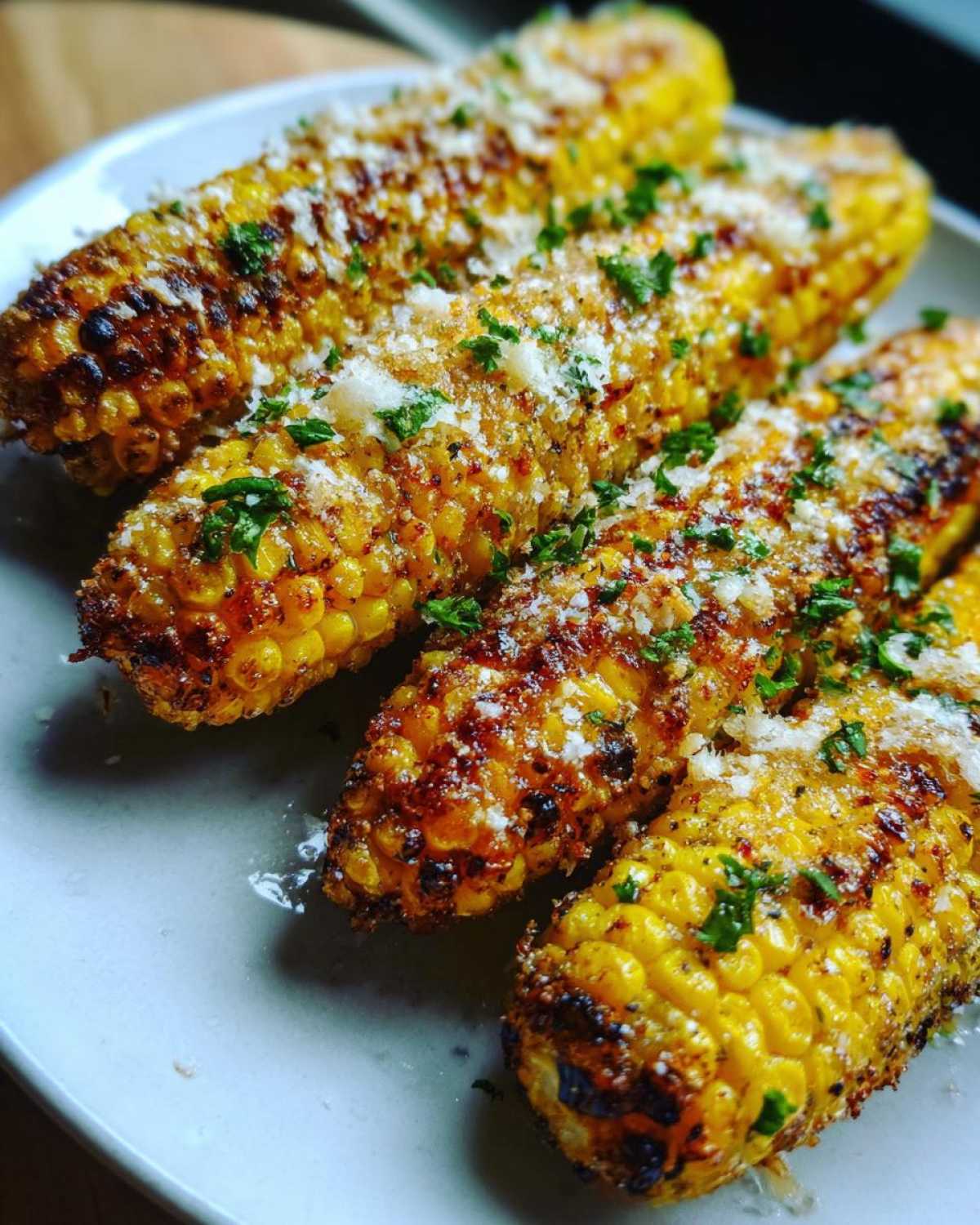 Close-up of four Air Fryer Crispy Parmesan Garlic Corn Ribs, charred and topped with grated Parmesan and parsley.