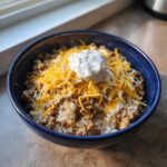 A close-up of an Air Fryer Crispy Turkey Taco Bowl layered with rice, seasoned ground turkey, shredded cheese, and sour cream.
