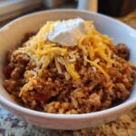 A white bowl filled with Air Fryer Crispy Turkey Taco Bowls, topped with shredded cheddar cheese and sour cream.