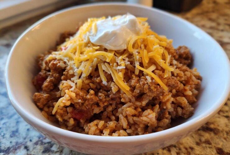 A white bowl filled with Air Fryer Crispy Turkey Taco Bowls, topped with shredded cheddar cheese and sour cream.