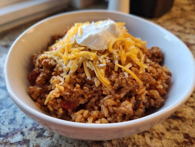 A white bowl filled with Air Fryer Crispy Turkey Taco Bowls, topped with shredded cheddar cheese and sour cream.