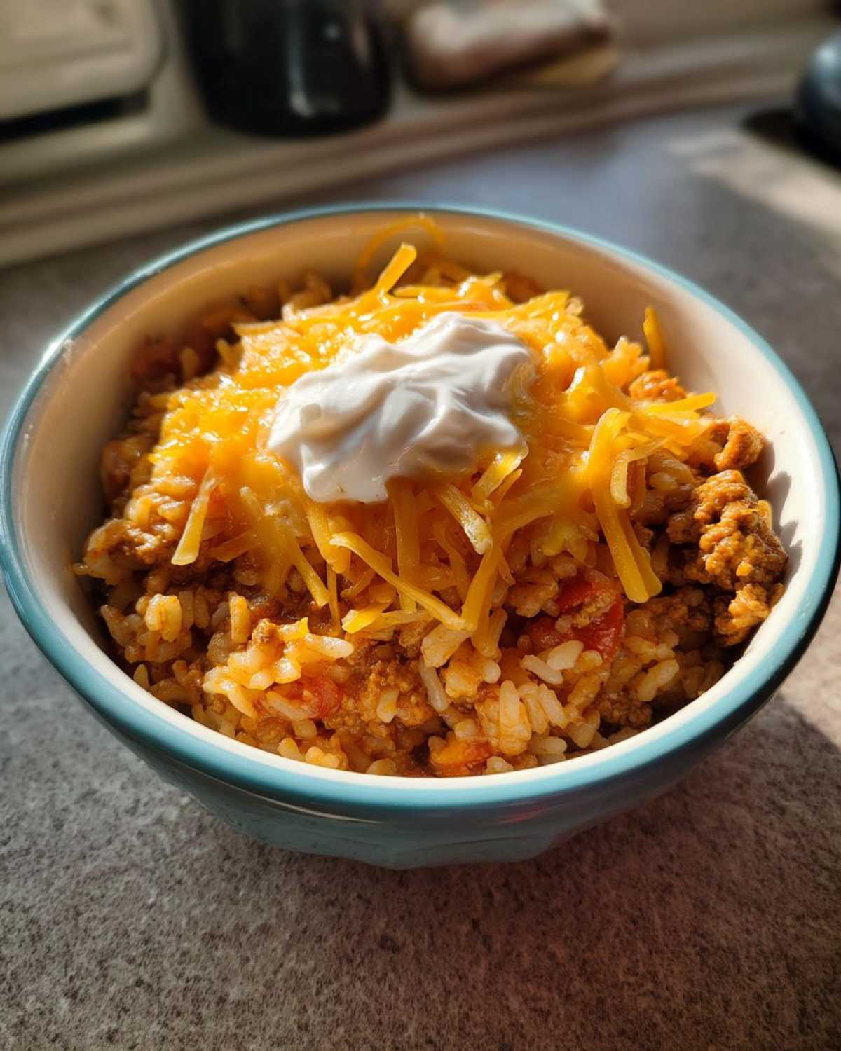 Close-up of a serving of Air Fryer Crispy Turkey Taco Bowls topped with shredded cheese and sour cream.