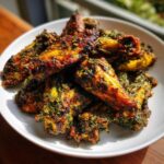 A pile of golden brown, crispy Air Fryer Crispy Zaatar Chicken Wings coated heavily in green zaatar seasoning on a white plate.