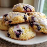 A stack of soft, golden Blueberry Cookies Lemon Glaze drizzled with white icing on a white plate.