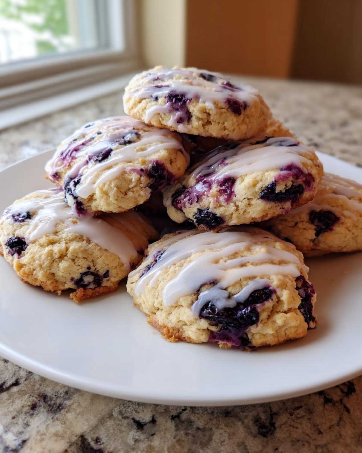 A stack of freshly baked Blueberry Cookies Lemon Glaze drizzled with white icing, piled on a white plate.