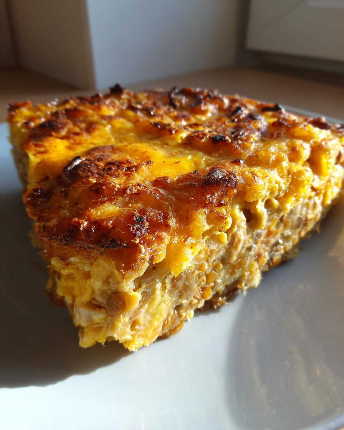 Close-up of a thick slice of Cheesy Lentil Bake Comfort Food showing a golden, browned, cheesy top layer and hearty lentil filling.