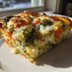 A close-up slice of Cheesy Veggie Quinoa Casserole featuring visible quinoa, bright orange carrots, and browned broccoli florets under melted cheese.