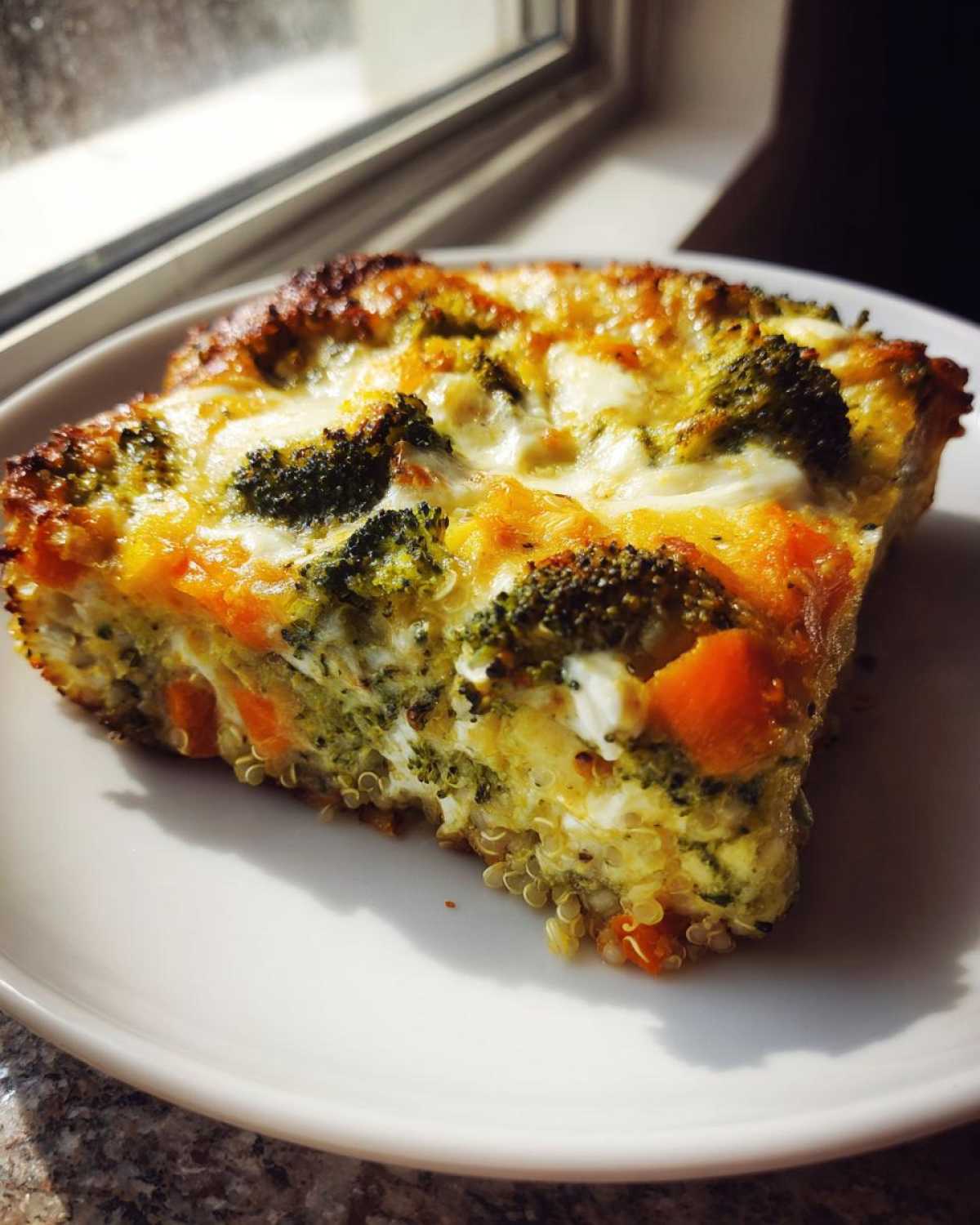A close-up slice of Cheesy Veggie Quinoa Casserole featuring visible quinoa, broccoli florets, and melted cheese.