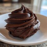 A perfect swirl of rich, dark Chocolate Buttercream Frosting piped onto a small white plate.