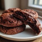 A stack of rich, dark Chocolate Chocolate Chip Cookies with one broken open to show the gooey, melted chocolate center.