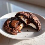 A rich, dark Chocolate Marshmallow Swirl Cookie cut in half, showing melted chocolate and gooey marshmallow filling.