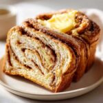A thick slice of homemade Cinnamon Swirl Bread topped with melting butter on a small plate.