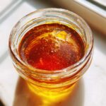 Close-up of rich, amber liquid, likely the finished Copycat Apple Cider Vinaigrette, settled in a small glass jar.