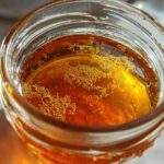 Close-up, top-down view of amber-colored Copycat Apple Cider Vinaigrette liquid with small bubbles in a glass jar.