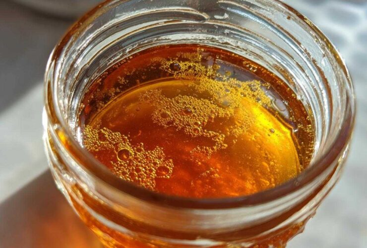 Close-up, top-down view of amber-colored Copycat Apple Cider Vinaigrette liquid with small bubbles in a glass jar.