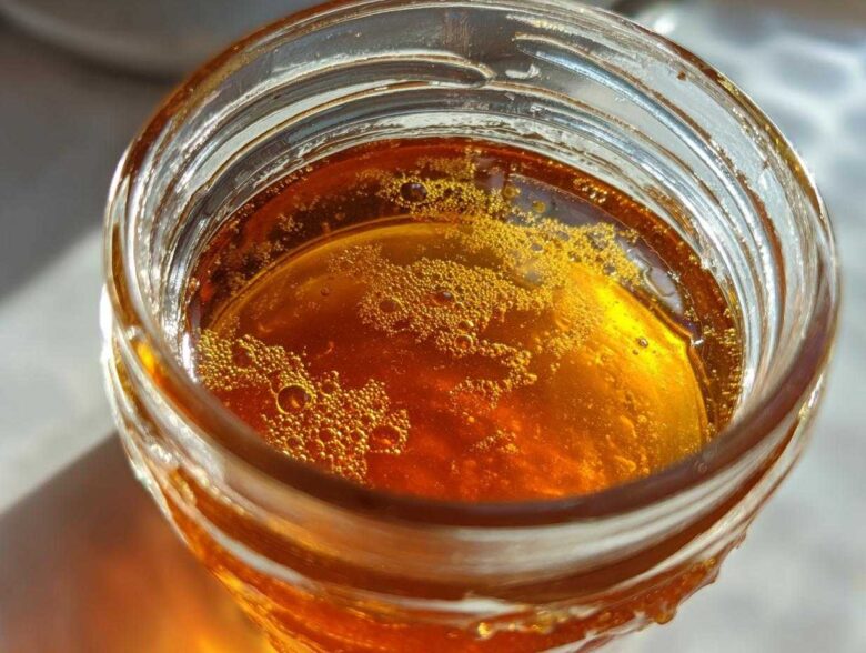 Close-up, top-down view of amber-colored Copycat Apple Cider Vinaigrette liquid with small bubbles in a glass jar.