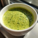 Close-up of vibrant green Copycat Green Goddess Ranch Dressing speckled with herbs in a small white ramekin.