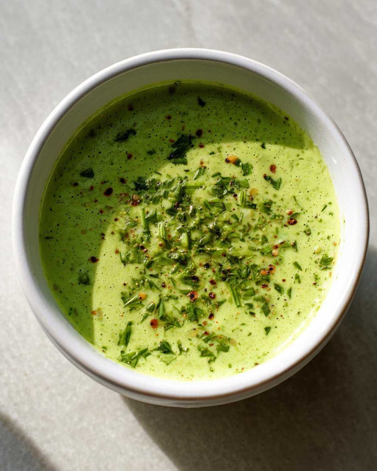 Overhead shot of thick, vibrant green Copycat Green Goddess Ranch Dressing topped with fresh herbs and pepper flakes in a white bowl.