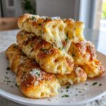 A stack of golden Copycat Italian Restaurant Soft Garlic Breadsticks with melted cheese pulling apart, sprinkled with Parmesan and parsley.