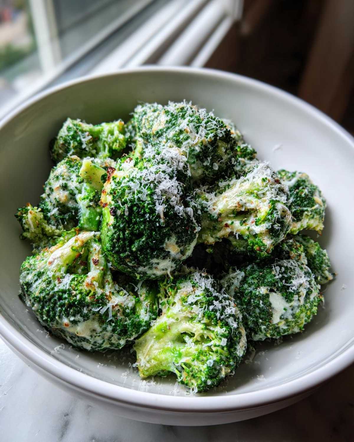 Bright green broccoli florets coated in a creamy sauce and topped with grated parmesan cheese, ready to eat.