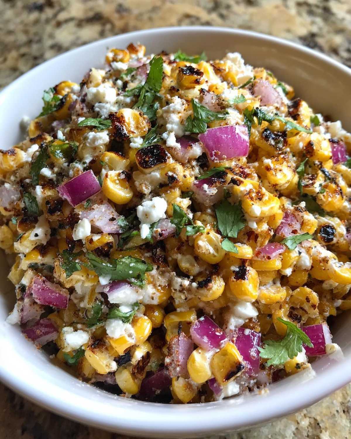 Close-up of charred corn kernels mixed with red onion, cotija cheese, and cilantro in a bowl of Copycat Mexican Grill Corn Salsa.