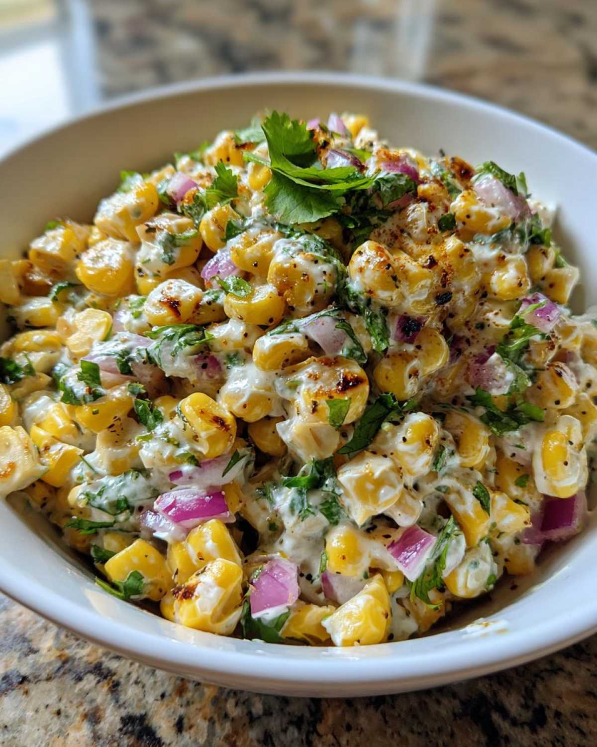 A close-up of creamy Copycat Mexican Grill Corn Salsa featuring charred corn, red onion, cilantro, and spices in a white bowl.
