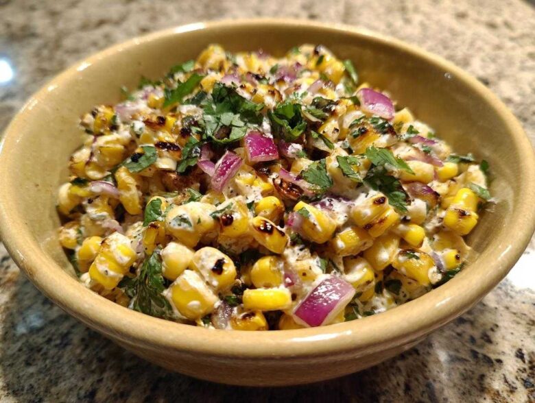 A close-up view of creamy, charred corn kernels mixed with red onion and cilantro, representing the Copycat Mexican Grill Corn Salsa.