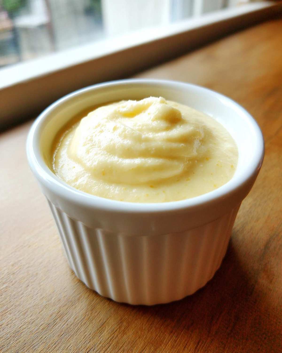 A small white ramekin filled with thick, creamy Copycat Pizza Garlic Parmesan Dip Sauce, set on a wooden surface.