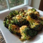 Close-up of bright green, crispy air fryer broccoli parmesan florets piled on a white square plate.