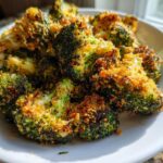 Close-up of crispy air fryer broccoli parmesan florets piled high on a white plate.