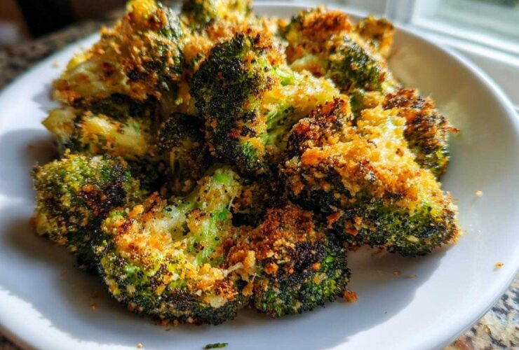 Close-up of crispy air fryer broccoli parmesan florets piled high on a white plate.