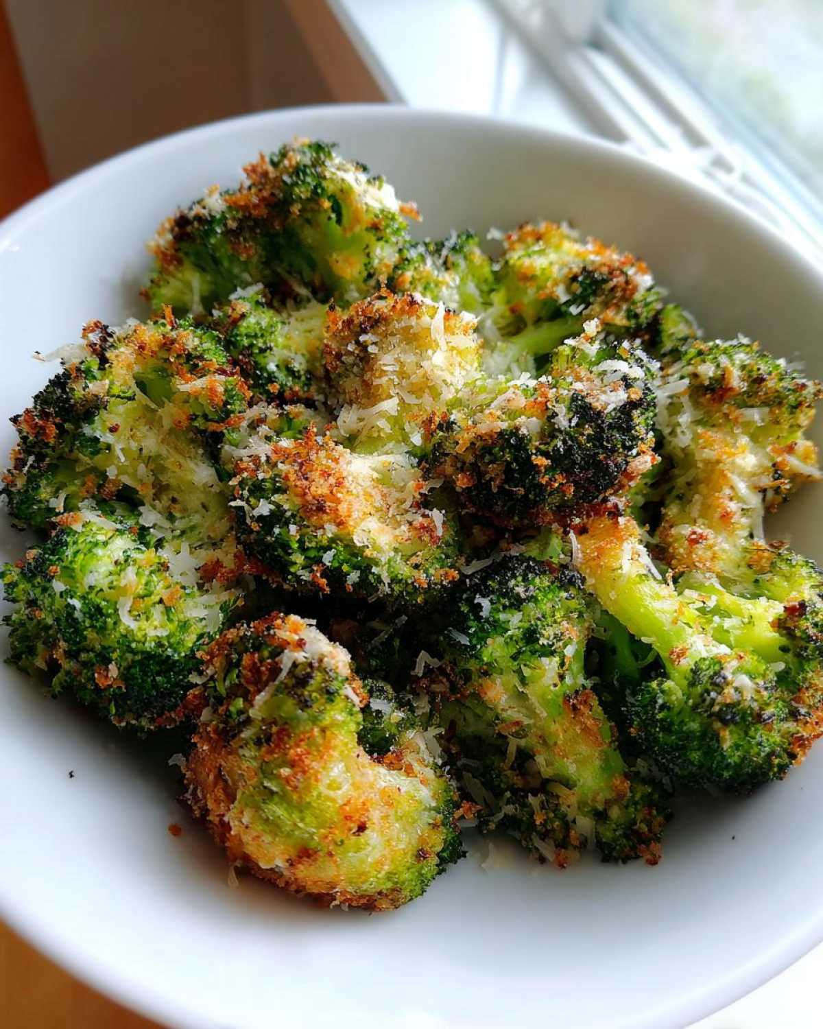 Close-up of Crispy Air Fryer Broccoli Parmesan florets topped with grated cheese in a white bowl.