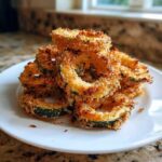 A stack of golden brown, crispy baked parmesan zucchini rings served on a white plate.
