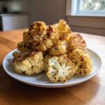 A pile of golden brown, perfectly Crispy Roasted Cauliflower florets served on a white plate.