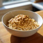 A white bowl filled with noodles topped generously with thick, creamy Easy 5-Minute Peanut Sauce.