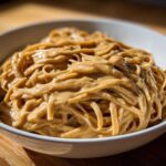 A close-up of noodles generously coated in a creamy, rich Easy 5-Minute Peanut Sauce, served in a white bowl.