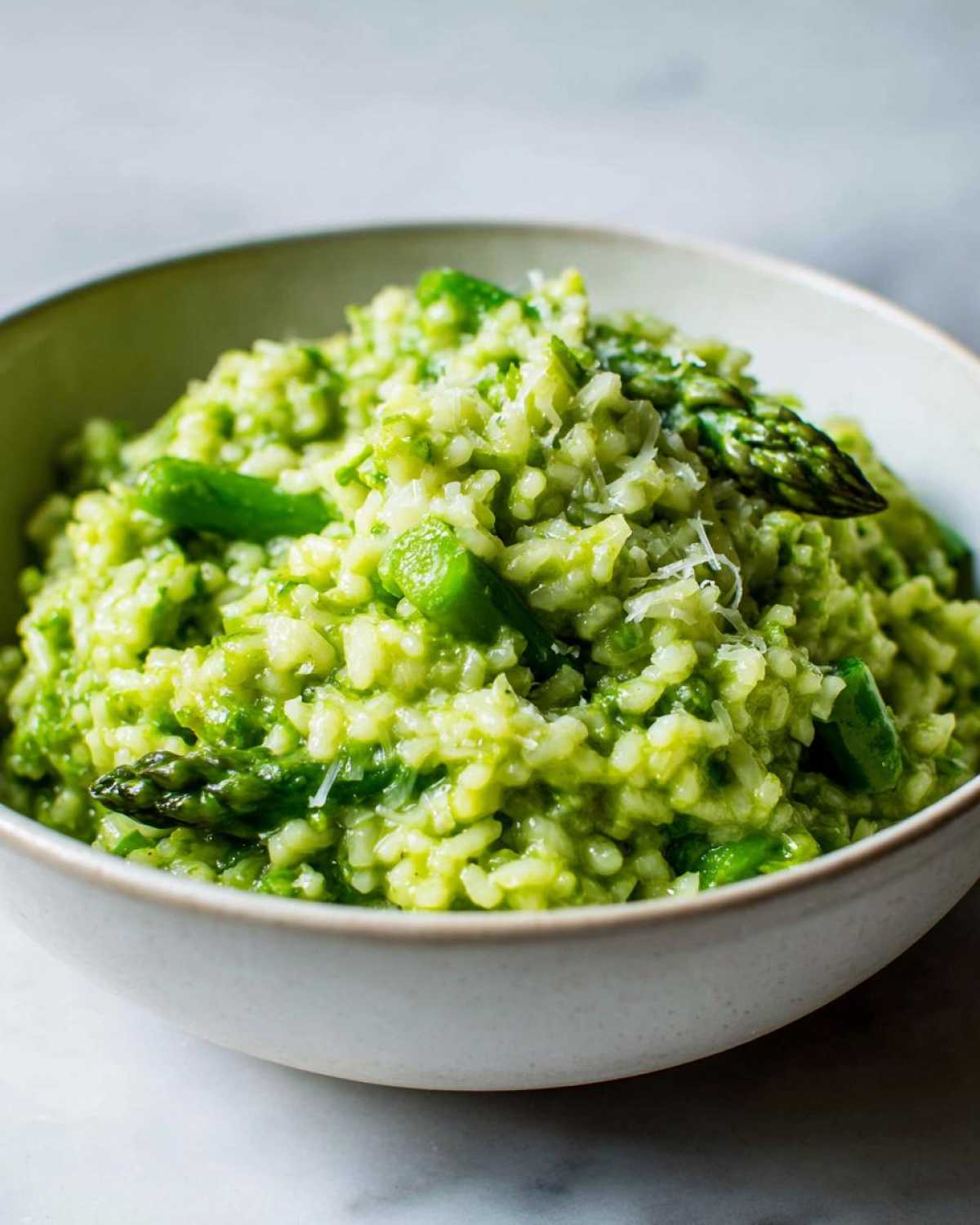 A close-up of a bowl filled with vibrant green Easy Creamy Asparagus Risotto, topped with Parmesan.