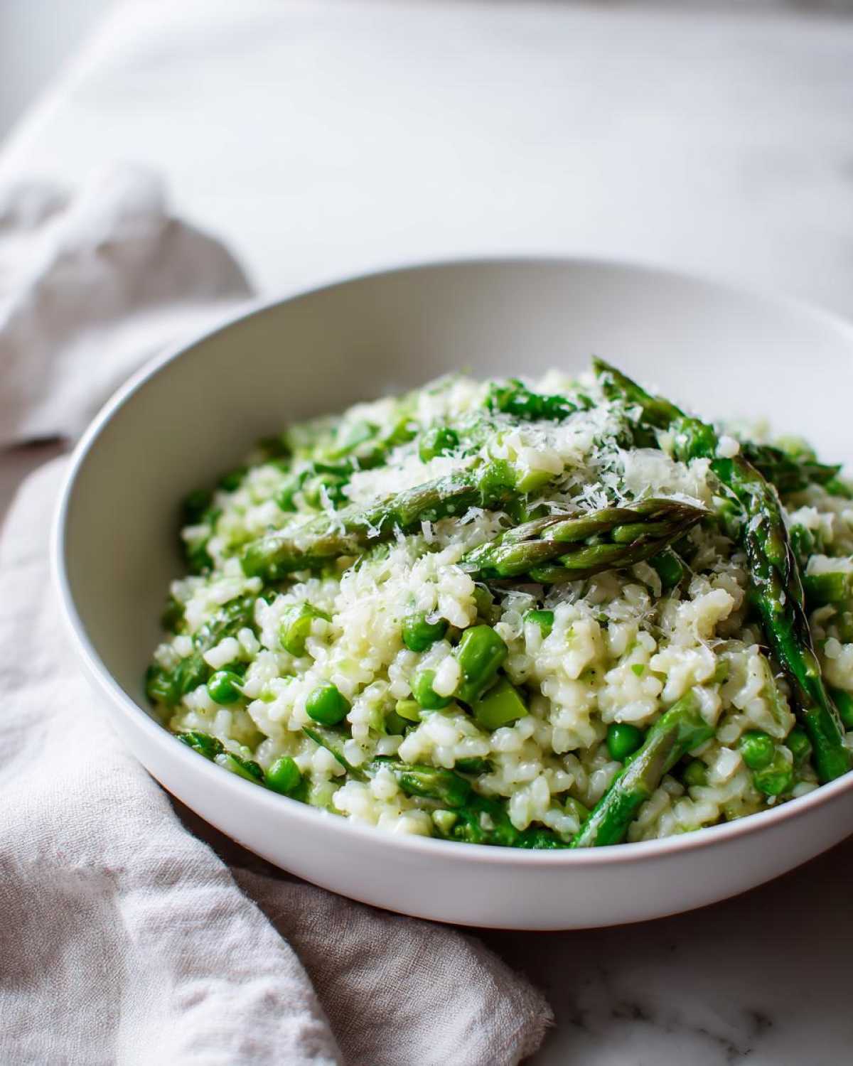 A white bowl filled with Easy Creamy Asparagus Risotto, topped with fresh asparagus spears and grated Parmesan cheese.