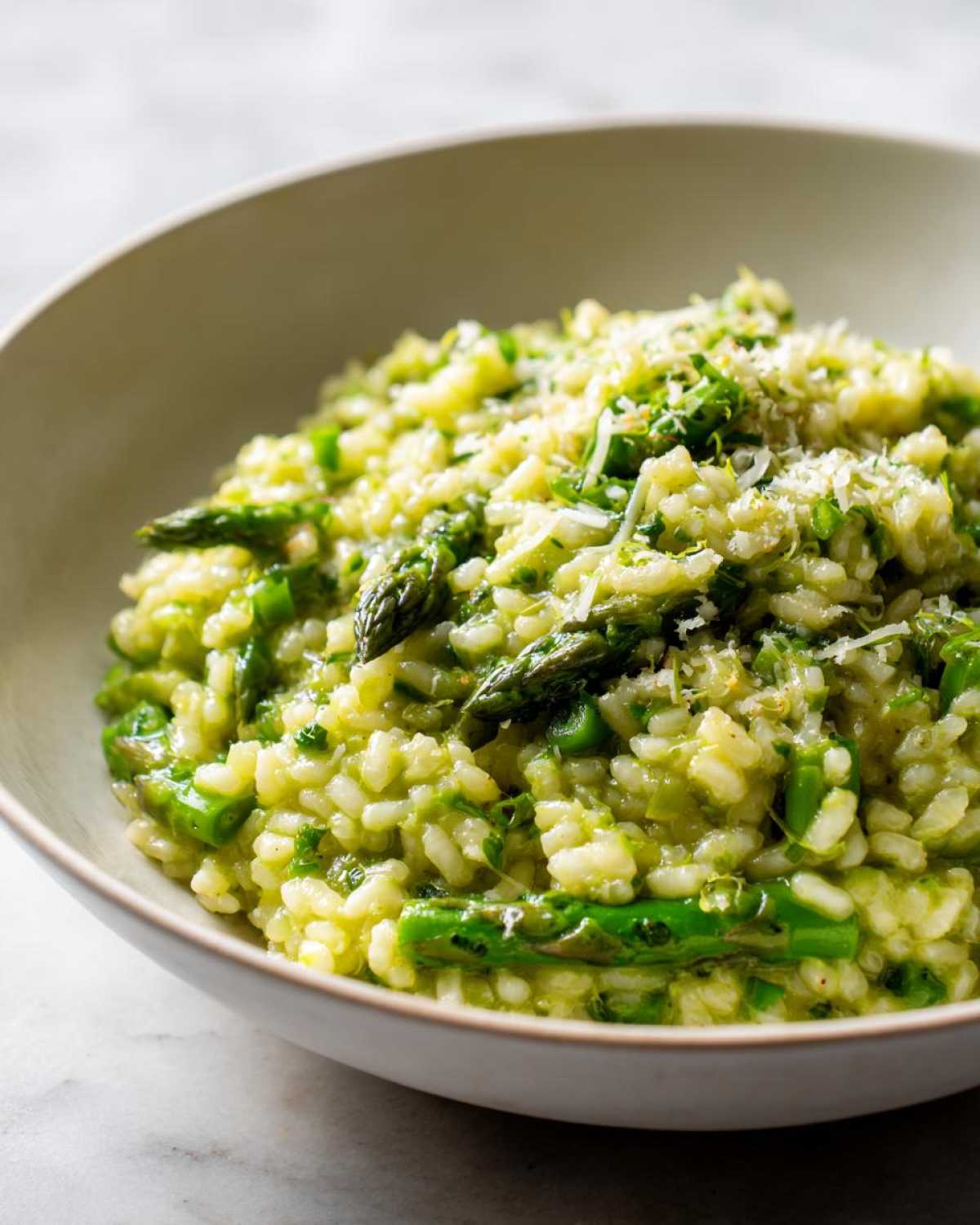 A close-up of a bowl filled with Easy Creamy Asparagus Risotto, topped with grated Parmesan cheese.