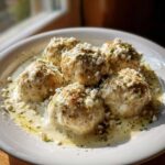 Close-up of five Easy Creamy Greek Chicken Meatballs served in a rich sauce and topped with crumbled feta cheese and herbs.