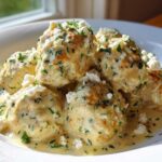 A bowl of Easy Creamy Greek Chicken Meatballs covered in a light sauce and topped with crumbled feta and fresh herbs.