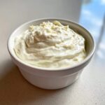 A close-up of thick, creamy Easy Greek Yogurt Caesar Dressing topped with grated cheese in a small white bowl.
