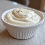 A close-up of thick, creamy Easy Greek Yogurt Caesar Dressing swirled in a small white ramekin.