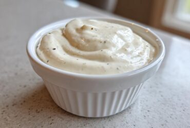 A close-up of thick, creamy Easy Greek Yogurt Caesar Dressing swirled in a small white ramekin.