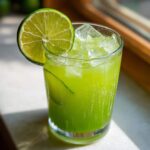 A tall glass filled with bright green Easy Iced Cucumber Lime Agua Fresca, ice, and garnished with a lime wheel.